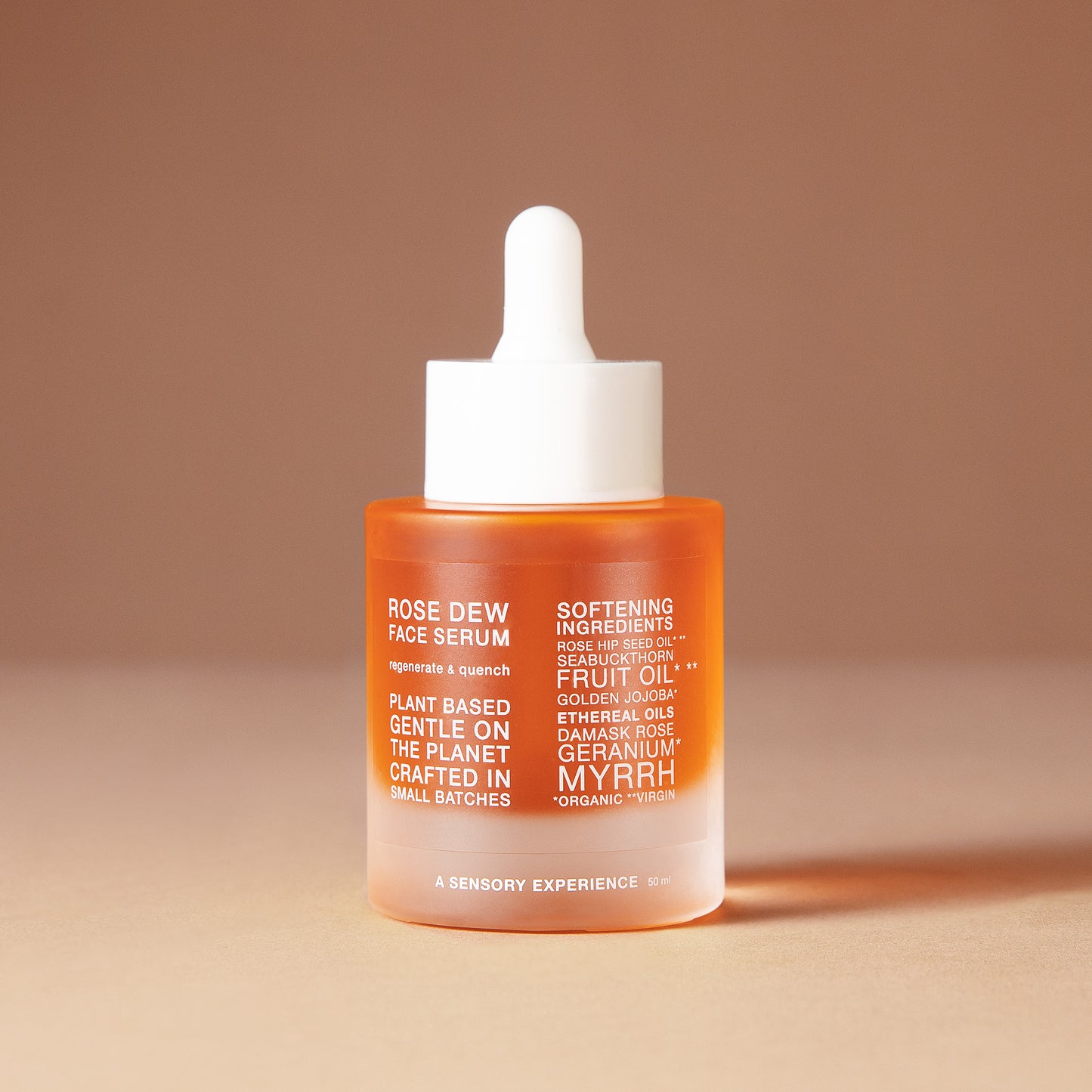A 50 ml bottle of DEAR BOTANICS artesian skincare face serum with a white dropper cap and a frosted glass bottle showing orange liquid inside, set against a warm beige background.