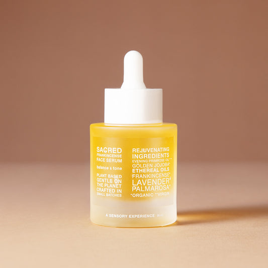 A 50 ml bottle of DEAR BOTANICS Artisanal Skincare face serum with a white dropper cap and a frosted glass bottle showing a golden-yellow liquid inside, set against a warm beige background.