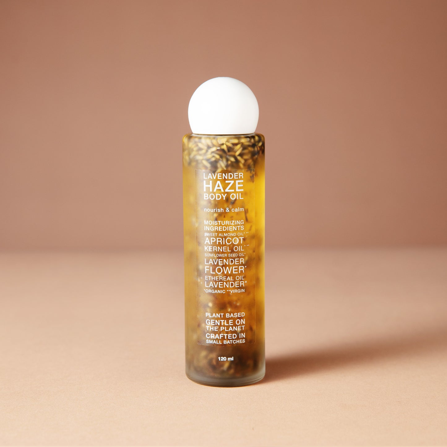 A clear cylindrical 120 ml bottle of DEAR BOTANICS essential oil diffuser liquid with visible botanical pieces inside, topped with a white spherical cap, set against a solid warm beige background.