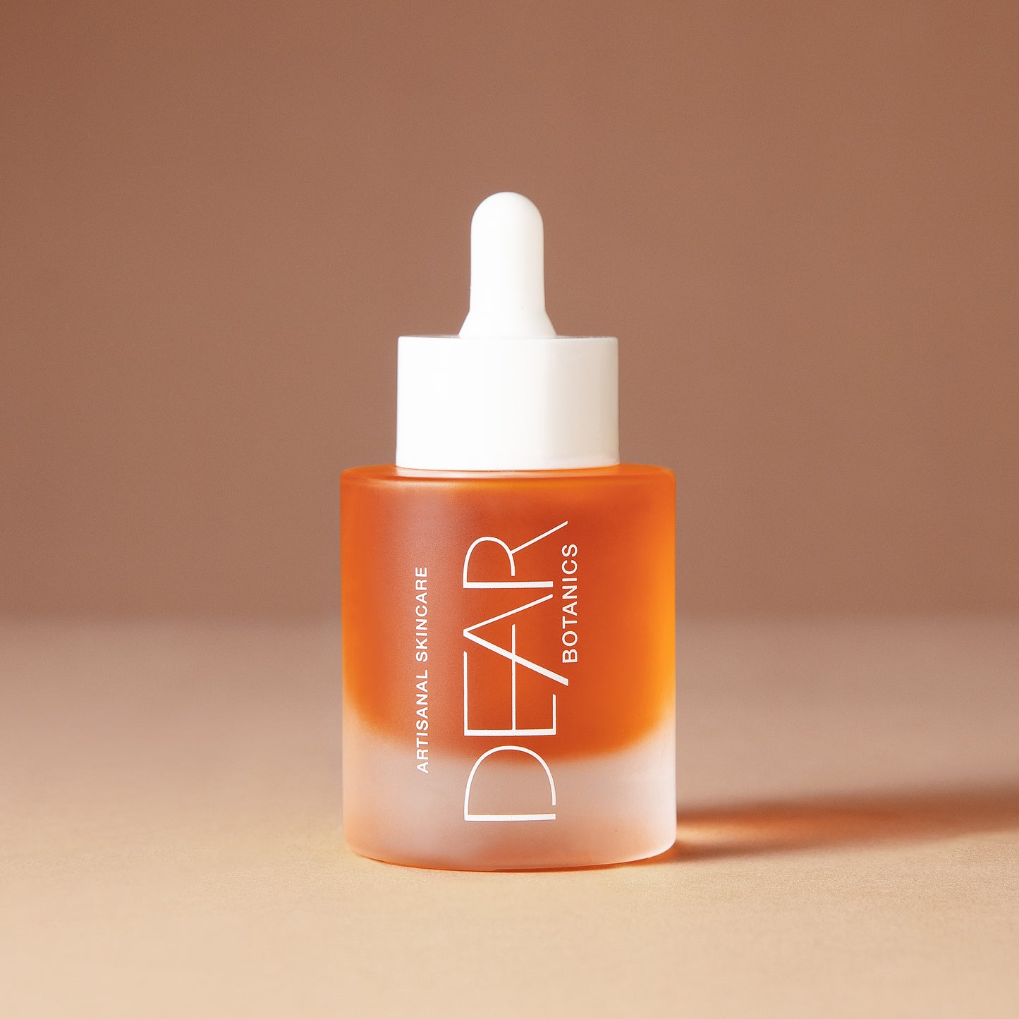 A 50 ml bottle of DEAR BOTANICS artesian skincare face serum with a white dropper cap and a frosted glass bottle showing orange liquid inside, set against a warm beige background.