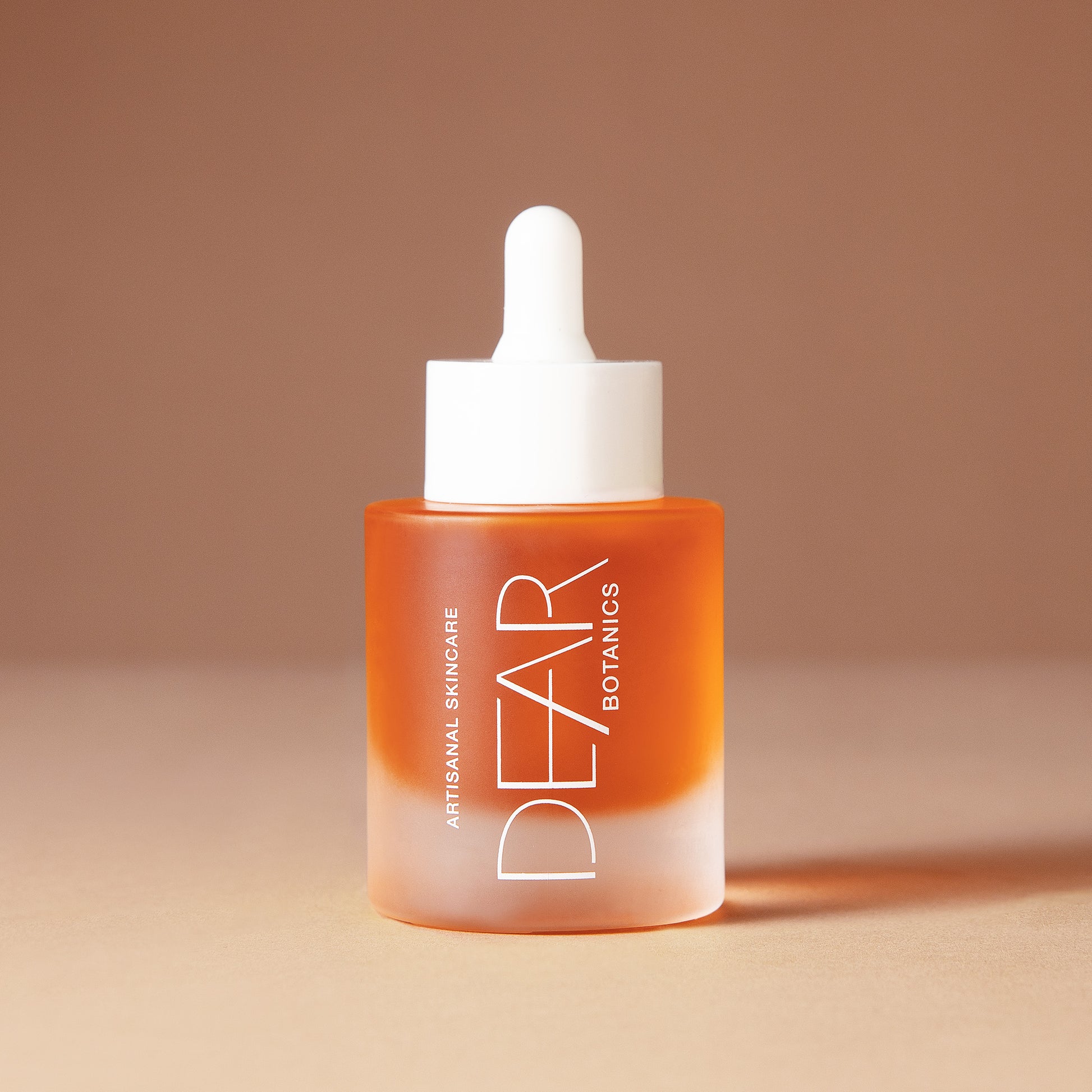 A 50 ml bottle of DEAR BOTANICS artesian skincare face serum with a white dropper cap and a frosted glass bottle showing orange liquid inside, set against a warm beige background.