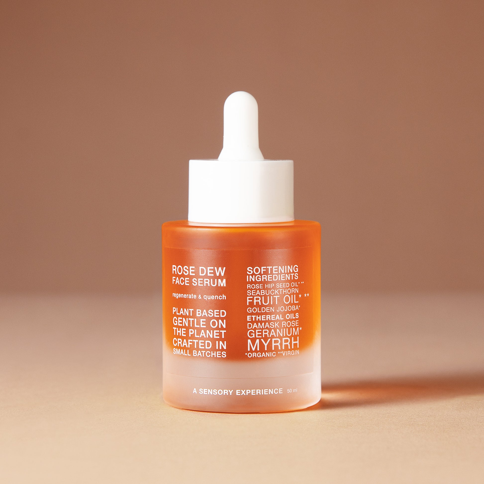 A 50 ml bottle of DEAR BOTANICS artesian skincare face serum with a white dropper cap and a frosted glass bottle showing orange liquid inside, set against a warm beige background.