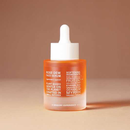 A 50 ml bottle of DEAR BOTANICS artesian skincare face serum with a white dropper cap and a frosted glass bottle showing orange liquid inside, set against a warm beige background.