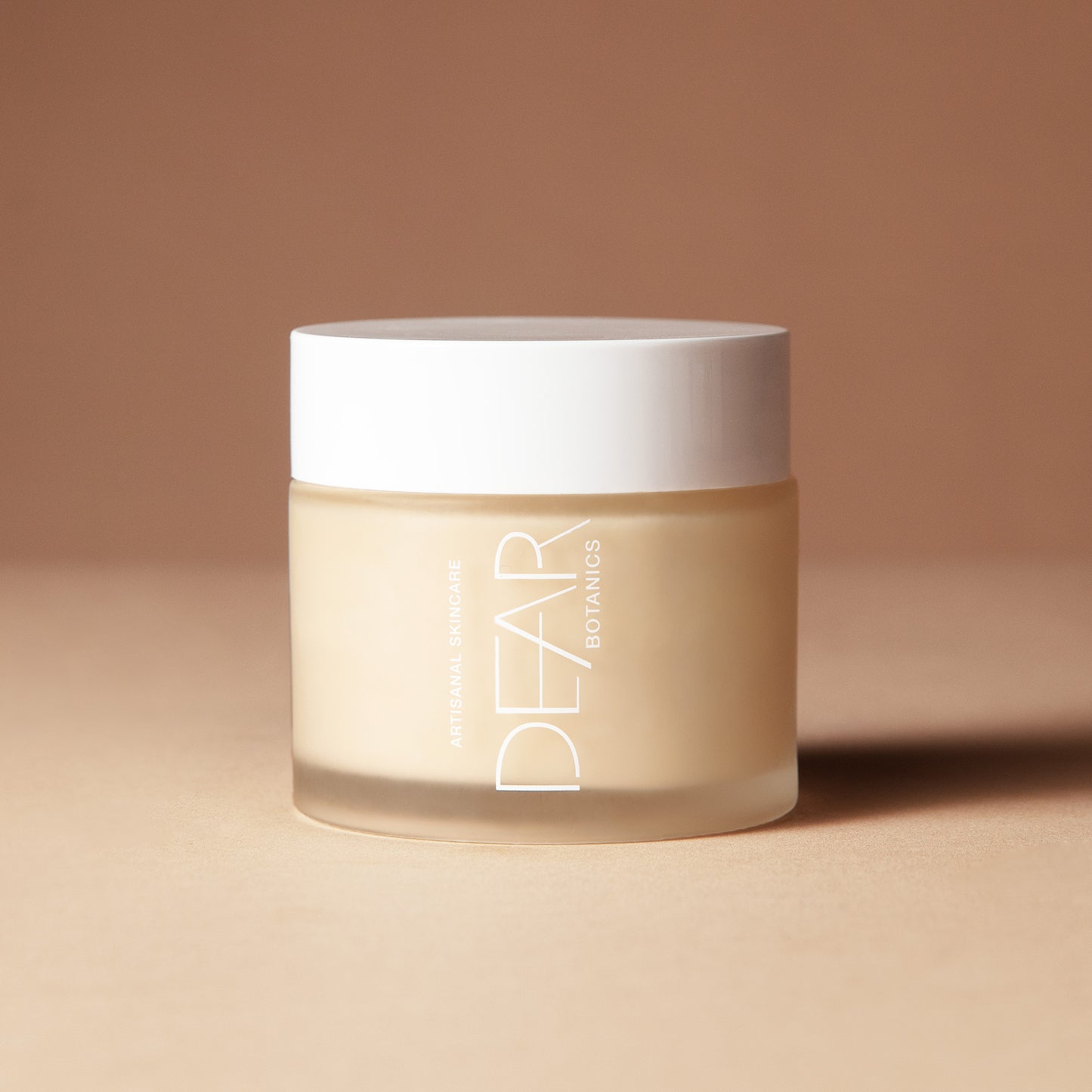 A 150 gram jar of DEAR BOTANICS shea butter cream, featuring a frosted beige glass container and a white lid, set against a warm beige background.
