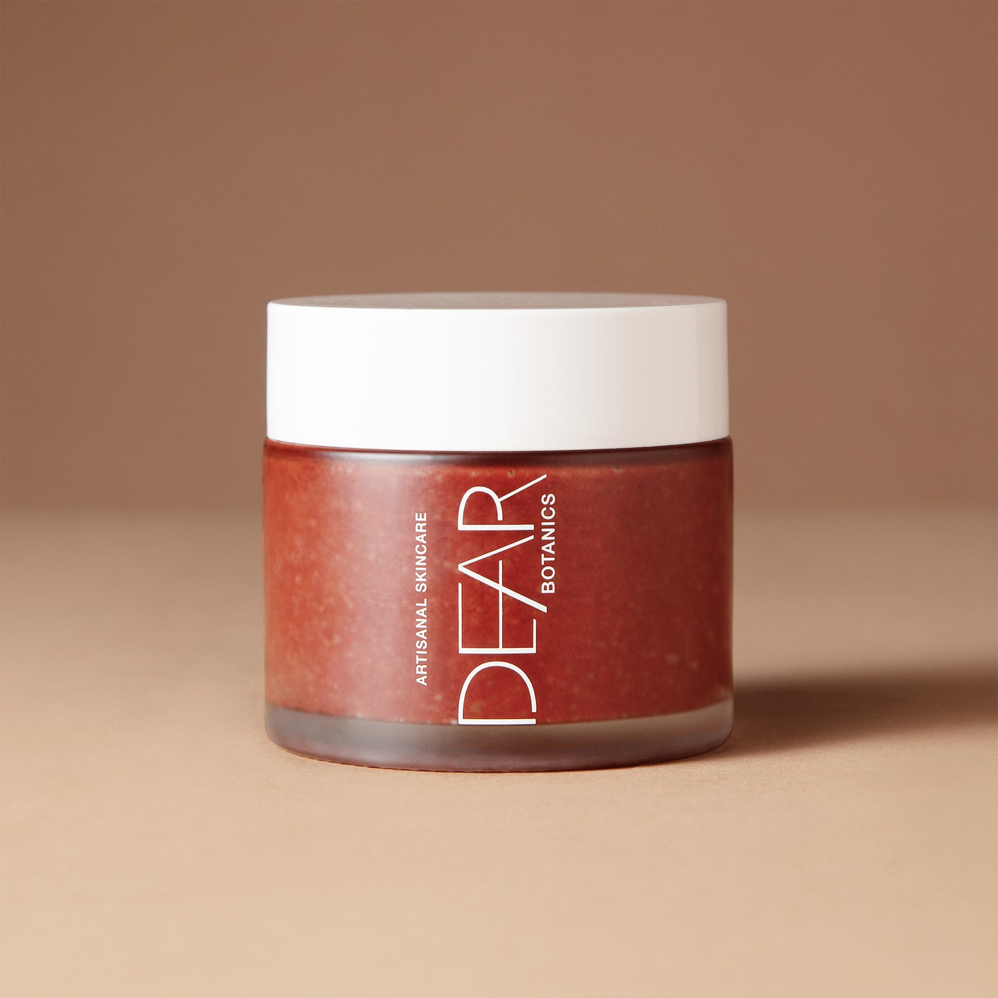 A 150 gram jar of DEAR BOTANICS Artisan Skincare Polish in a warm reddish-brown shade, featuring a white lid and white text on the front, set against a solid beige-brown background.
