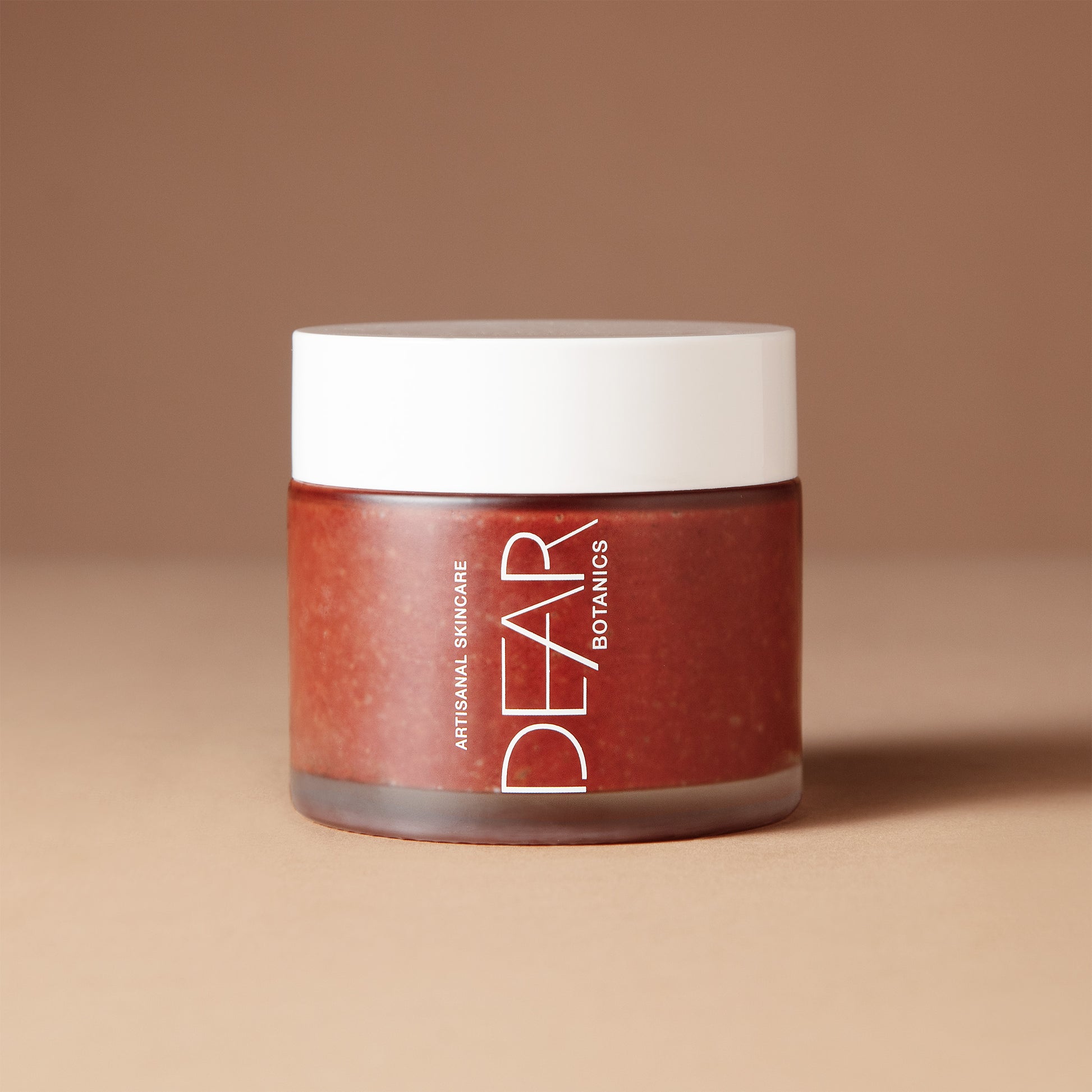 A 150 gram jar of DEAR BOTANICS Artisan Skincare Polish in a warm reddish-brown shade, featuring a white lid and white text on the front, set against a solid beige-brown background.