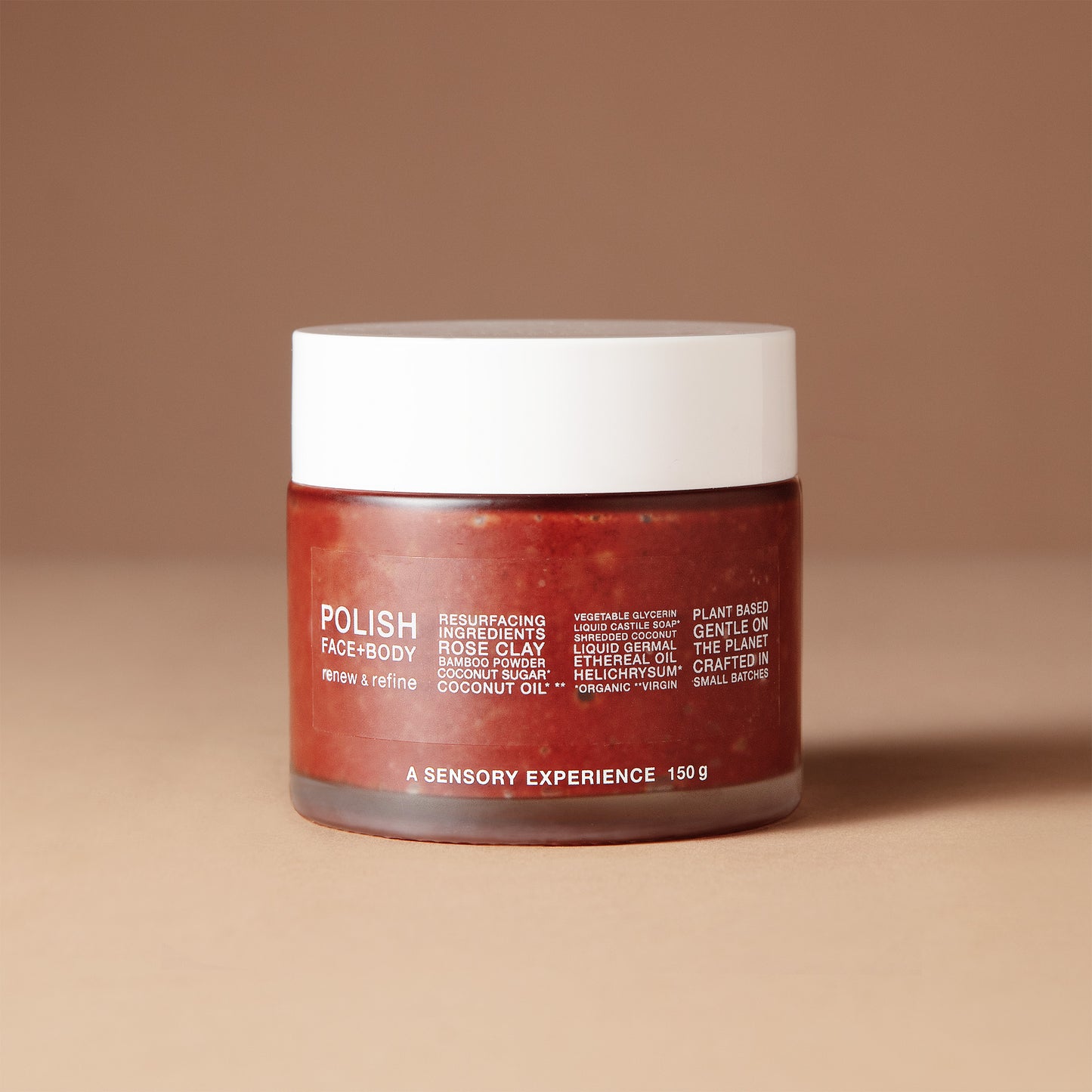 A 150 gram jar of DEAR BOTANICS Artisan Skincare Polish in a warm reddish-brown shade, featuring a white lid and white text on the front, set against a solid beige-brown background.